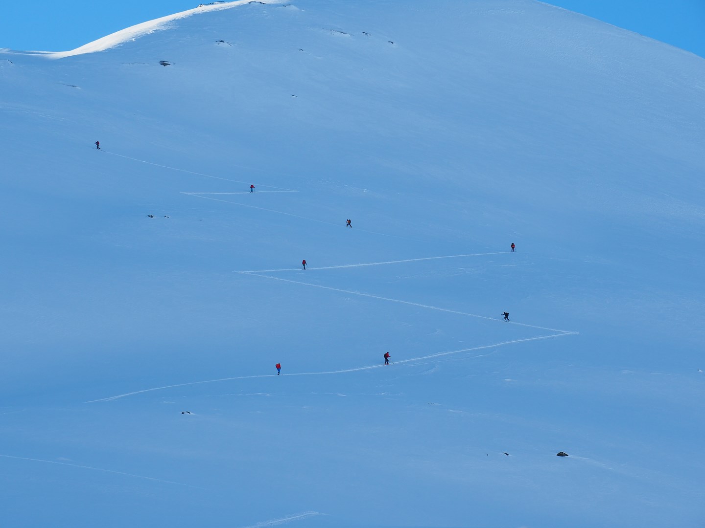 En gruppe skigåere beveger seg oppover en fjellside med god avlastningsavstand.