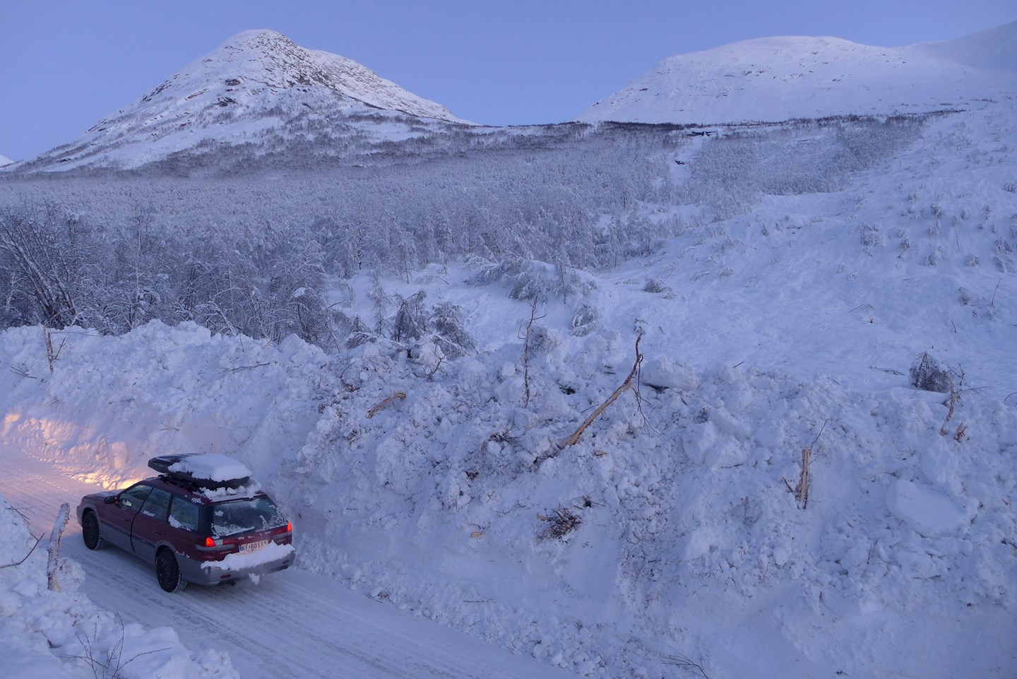En bil står parkert på en vei som tidligere har blitt truffet av et stort snøskred.